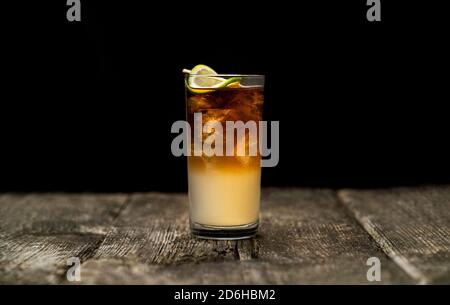 Cocktail sombre et orageux dans un verre à boule haute avec de la glace et une garniture de citron vert sur une vieille table en bois avec un fond noir Banque D'Images