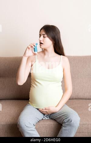 femme enceinte utilisant un inhalateur d'asthme pendant l'attaque pour être en bonne santé sur le canapé à la maison. Concept de soins de santé du millénaire en santé. Banque D'Images