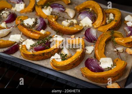 Tranches de citrouille ou de courge cuites avec oignons rouges, ail, fromage feta et thym sur un plateau, légumes d'automne pour un repas de Thanksgiving et d'Halloween, séle Banque D'Images