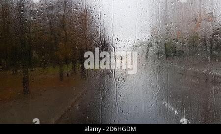 Pluie sur la vitre arrière d'une voiture en automne. Vue intérieure de la route avec des voitures en mouvement dans la ville par la fenêtre de la voiture avec gouttes de pluie Banque D'Images