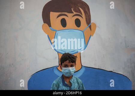 Gaza, Palestine. 17 octobre 2020. Un enfant palestinien portant un masque facial vu devant une murale représentant un enfant portant un masque sur un mur à Khan Yunis, au sud de la bande de Gaza. Crédit : Yousef Masoud/SOPA Images/ZUMA Wire/Alay Live News Banque D'Images