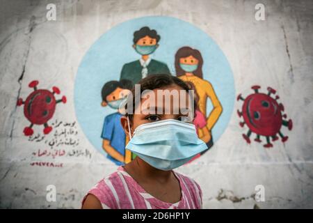 Gaza, Palestine. 17 octobre 2020. Une fille palestinienne portant un masque facial à côté d'une murale représentant des enfants portant un masque sur un mur à Khan Yunis, au sud de la bande de Gaza. Crédit : Yousef Masoud/SOPA Images/ZUMA Wire/Alay Live News Banque D'Images