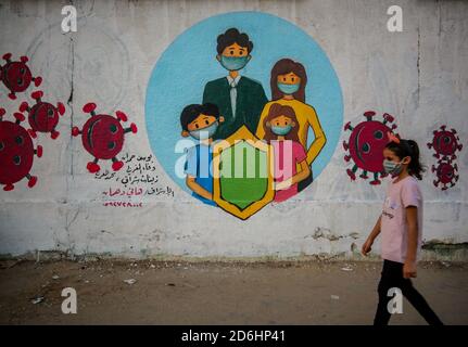 Gaza, Palestine. 17 octobre 2020. Une fille palestinienne qui marche devant une murale représentant des enfants portant un masque sur un mur à Khan Yunis, au sud de la bande de Gaza. Crédit : Yousef Masoud/SOPA Images/ZUMA Wire/Alay Live News Banque D'Images