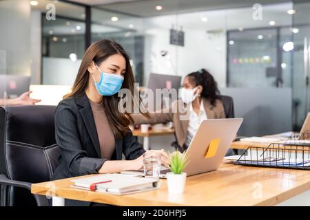 Portrait d'un employé de bureau asiatique femme d'affaires porter un masque de protection travailler dans un nouveau bureau normal avec une équipe interraciale en arrière-plan en tant que social dist Banque D'Images