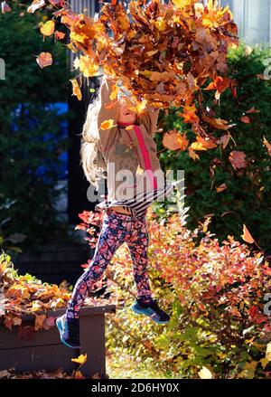 Une fille de 6 ans, sautant et jetant jouer avec les feuilles d'automne Banque D'Images