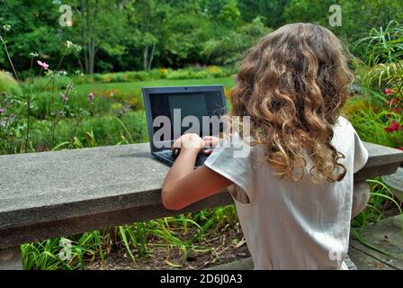 une jeune fille qui fait du travail à l'école sur un ordinateur d'apprentissage à distance dans le parc Banque D'Images