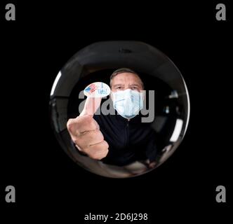 Homme âgé portant un masque facial contre le virus et montrant moi étiquette votée reflétée dans la boule de verre de la chance de dire Banque D'Images