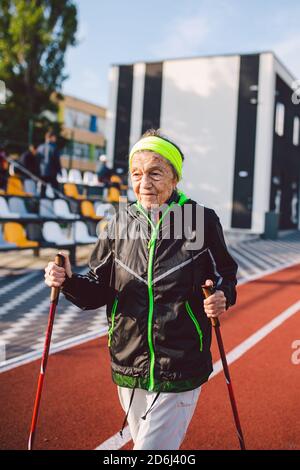 Femme âgée marchant avec des bâtons de marche dans le stade sur une couverture en caoutchouc rouge. Femme âgée de 88 ans effectuant des exercices de marche nordique à la ville Banque D'Images