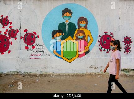 Une fille palestinienne qui marche devant une murale représentant des enfants portant un masque sur un mur à Khan Yunis, au sud de la bande de Gaza. Banque D'Images