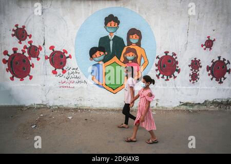 Des filles palestiniennes marchant devant une fresque représentant des enfants portant un masque sur un mur à Khan Yunis, au sud de la bande de Gaza. Banque D'Images