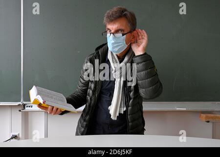 Professeur avec une veste d'hiver épaisse, foulard et masque facial en classe, main sur l'oreille, problèmes de communication, crise corona, Stuttgart, Baden-Wuerttemberg Banque D'Images