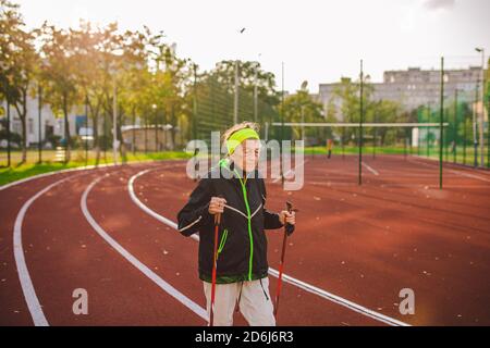 Femme âgée marchant avec des bâtons de marche dans le stade sur une couverture en caoutchouc rouge. Femme âgée de 88 ans effectuant des exercices de marche nordique à la ville Banque D'Images