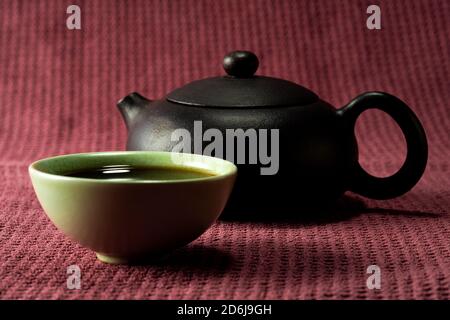 Thé chinois à la vapeur dans un petit thé vert isolé avec un arrière-plan noir et une surface rouge Banque D'Images