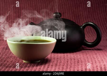 Thé chinois à la vapeur dans un petit thé vert isolé avec un arrière-plan noir et une surface rouge Banque D'Images