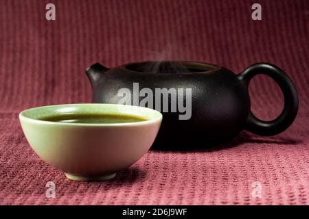 Thé chinois à la vapeur dans un petit thé vert isolé avec un arrière-plan noir et une surface rouge Banque D'Images