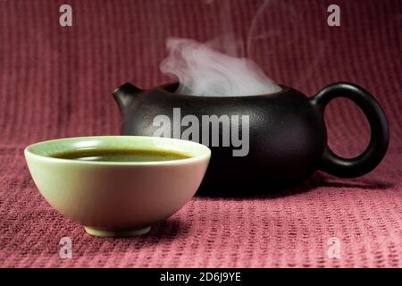 Thé chinois à la vapeur dans un petit thé vert isolé avec un arrière-plan noir et une surface rouge Banque D'Images
