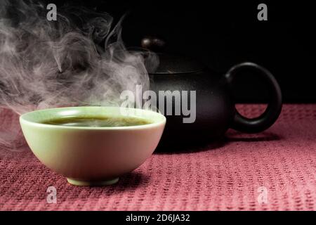 Thé chinois à la vapeur dans un petit thé vert isolé avec un arrière-plan noir et une surface rouge Banque D'Images