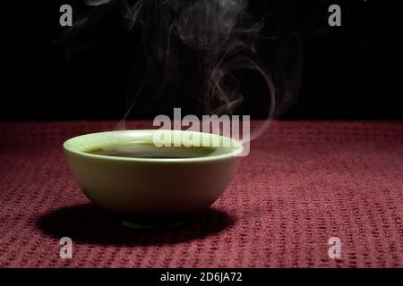 Thé chinois à la vapeur dans un petit thé vert isolé avec un arrière-plan noir et une surface rouge Banque D'Images