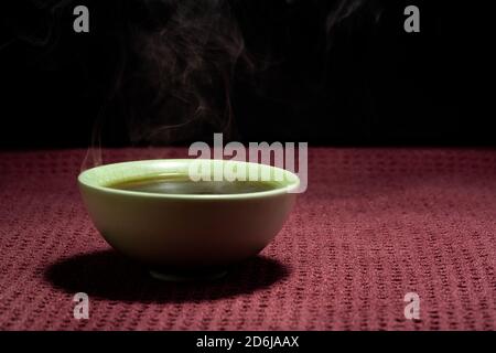 Thé chinois à la vapeur dans un petit thé vert isolé avec un arrière-plan noir et une surface rouge Banque D'Images