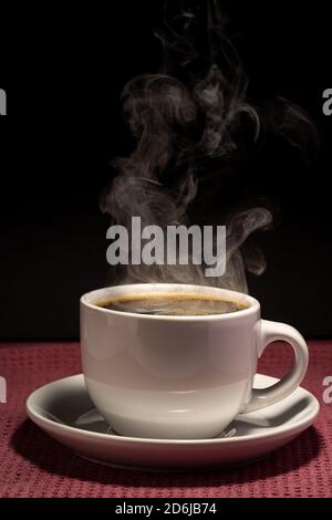 Café cuisant dans une tasse avec soucoupe isolée sur un arrière-plan noir sur une surface rouge Banque D'Images