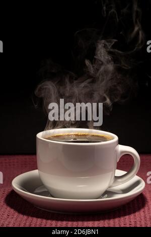 Café cuisant dans une tasse avec soucoupe isolée sur un arrière-plan noir sur une surface rouge Banque D'Images