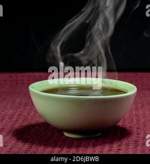 Thé chinois à la vapeur dans un petit thé vert isolé avec un arrière-plan noir et une surface rouge Banque D'Images