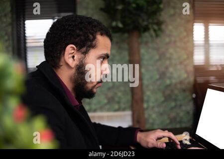 Jeune homme noir développeur assis dans un restaurant pizza, boire du café ou du thé et travailler avec un ordinateur portable. Banque D'Images