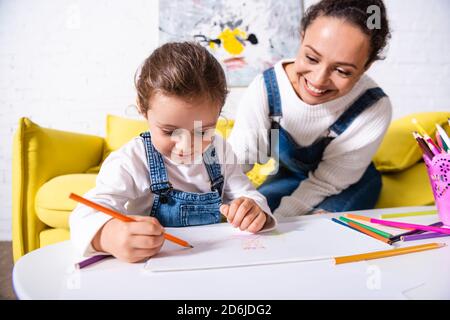 Fille dessin avec des crayons de couleur près de la mère à la maison Banque D'Images