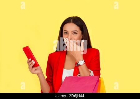 Portrait d'une femme assez excité avec des sacs colorés looking at mobile phone rire heureux fashion girl isolé sur fond jaune. Mul Banque D'Images