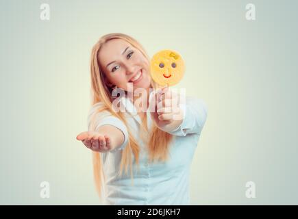 Femme blonde lumineuse proposant de donner un bâton de bonbon avec emoji lolipop sourire à la caméra isolée sur fond vert clair jaune avec espace de copie. Flou Banque D'Images