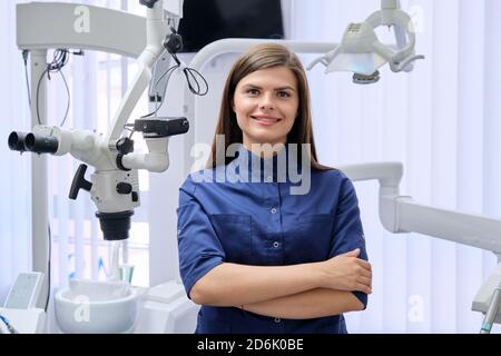 Portrait d'une jeune femme médecin dentiste confiante avec les mains pliées dans le cabinet dentaire. Banque D'Images