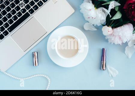 Espace de travail féminin au plafond avec une tasse de café, des fleurs de pivoine, un carnet, un casque, une nappe bleu clair et des accessoires. Bureau à domicile élégant. Confortable maison, hygge, concept d'été. Planification du matin. Banque D'Images