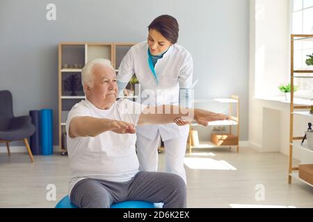 Une kinésithérapeute féminine forme un homme âgé dans la chambre en soutenant ses bras étirés. Banque D'Images