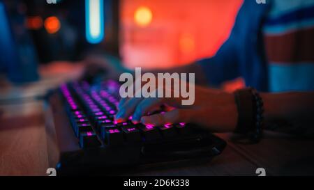 Gros plan des mains montrant un joueur en appuyant sur les boutons du clavier tout en jouant à un jeu vidéo en ligne. Voyants du clavier. Le joueur porte un bracelet Banque D'Images