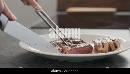 Homme en tranches de steak de ribeye sur une assiette blanche sur un comptoir en béton, photo large Banque D'Images