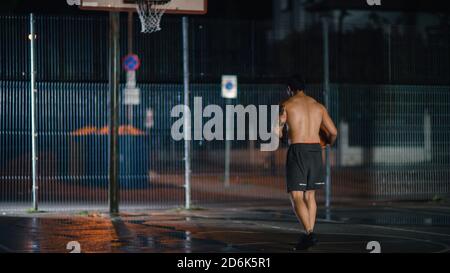 Le joueur de basket-ball masculin jeune sportif dribbles et jette le ballon en position de crouped dans un quartier résidentiel clôturé terrain de Streetball. Banque D'Images