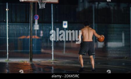 Le joueur de basket-ball masculin jeune sportif dribbles et jette le ballon en position de crouped dans un quartier résidentiel clôturé terrain de Streetball. Banque D'Images