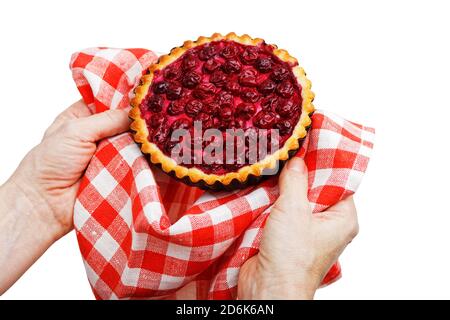 Les mains du chef tiennent le tartelet fraîchement cuit avec une cerise dans une serviette rouge et blanche. Isolé sur blanc. Banque D'Images