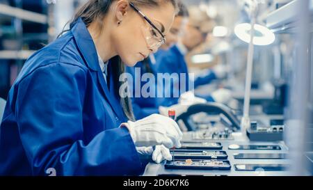 Femmes ouvriers d'usine d'électronique en Blue Work Coat et lunettes de protection montage de cartes de circuit imprimé pour smartphones avec brucelles. Haute technologie Banque D'Images