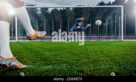 Le joueur de football anonyme lance le ballon sur la pénalité, le gardien de but professionnel se tient dans les buts, saute pour attraper le ballon. Banque D'Images