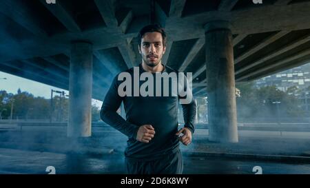 Portrait prise d'un jeune homme athlétique musclé dans un ensemble de sport jogging dans la rue. Il court dans un environnement urbain sous un pont. Banque D'Images