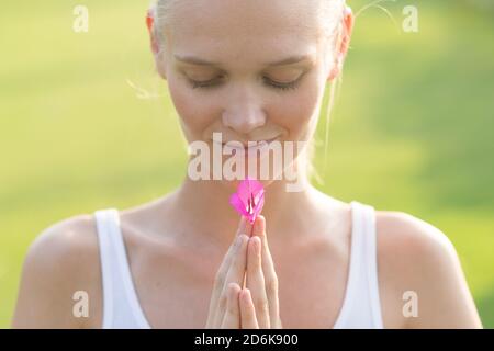 Bien-être et détente. Jeune femme calme tenant une fleur rose dans ses mains contre un fond vert. Banque D'Images