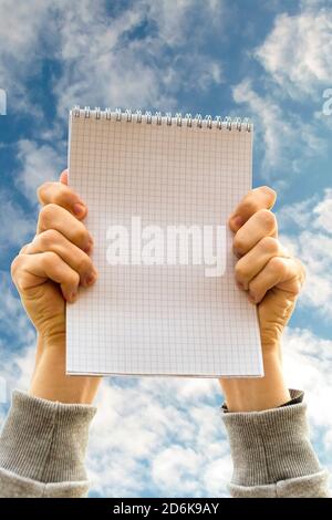 Mains tenant un carnet à l'opposé bleu ciel nuageux Banque D'Images