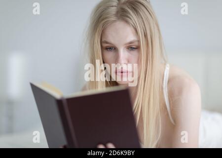 Jeune femme concentrée lisant un livre au lit le matin. Banque D'Images