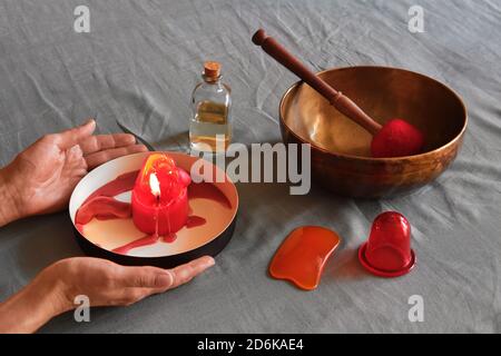 Articles de massage : huile, bol de chant, aspirateur sur toile de fond. Mains de femme tenant une bougie d'arôme brûlante Banque D'Images