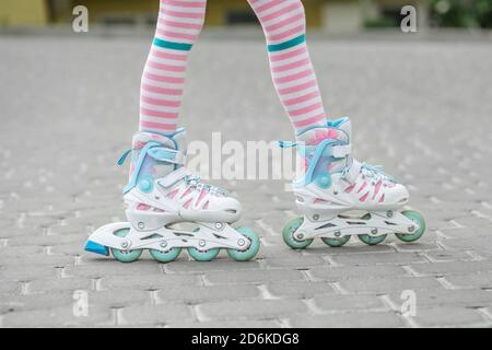 L'enfant apprend à faire du patin à roulettes. Collants roses pour fille. Concept d'enfance et de passe-temps. Banque D'Images