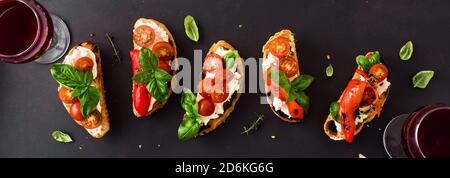 Sandwichs à la bruschetta avec tomates, fromage à la crème, paprika grillé et basilic sur fond sombre, vue du dessus, bannière. En-cas italien traditionnel pour le vin Banque D'Images
