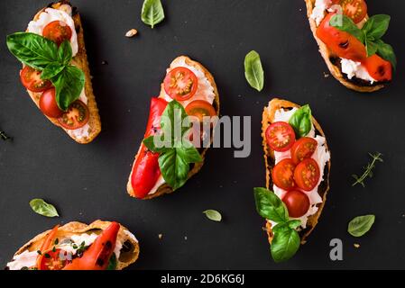 Sandwichs à la bruschetta avec tomates, fromage à la crème, paprika grillé et basilic sur fond sombre, vue du dessus, espace de copie. En-cas italien traditionnel - gri Banque D'Images