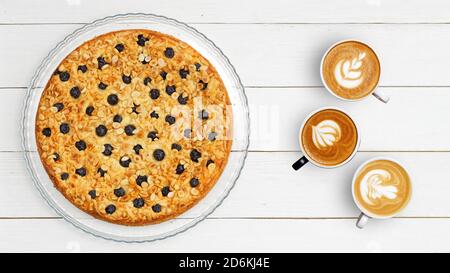 Trois tasses de café et un gâteau fait maison décoré d'amandes et de bleuets sur une table en bois blanc. Vue de dessus. CopySpace. Banque D'Images
