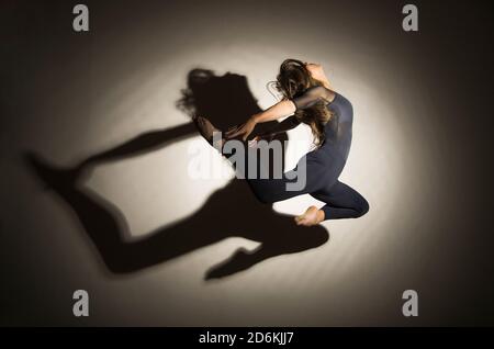la femme dans l'obscurité effectue le saut de gymnastique, sur un fond blanc il y a une ombre d'une forme. Photographie en studio. Banque D'Images